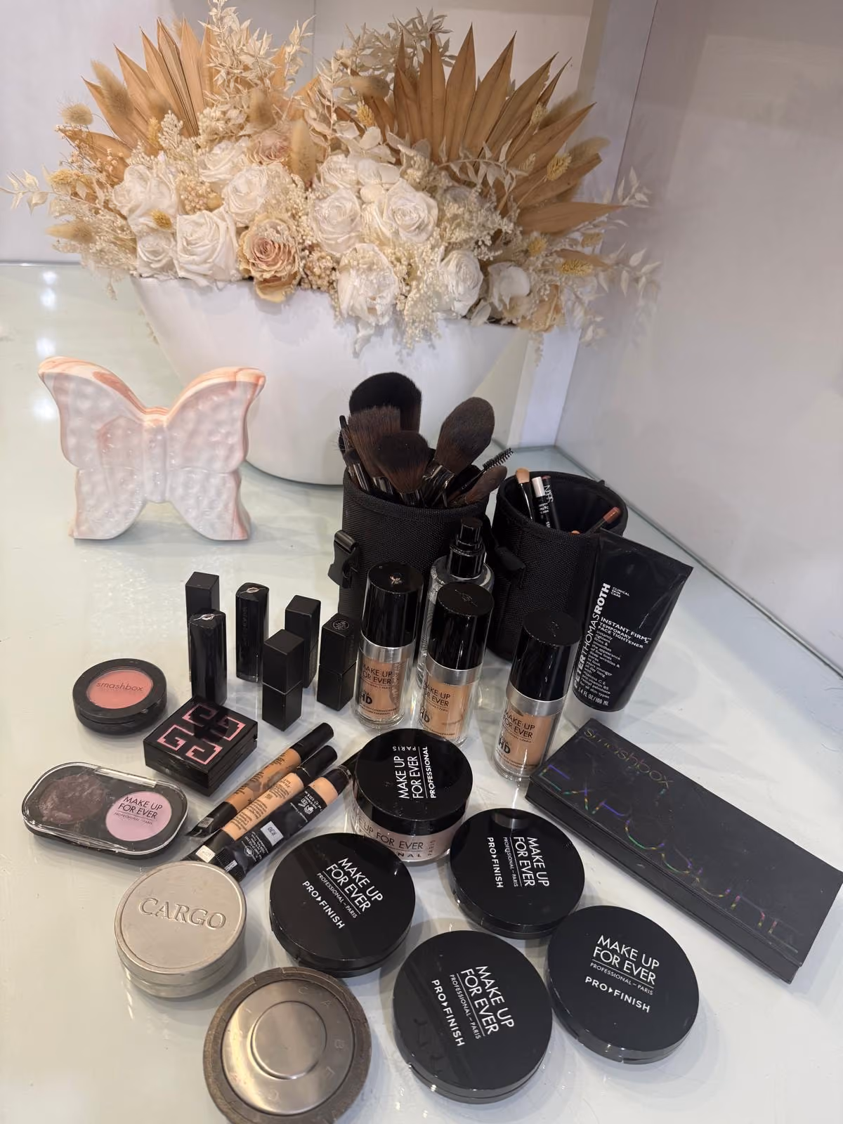 The salon's makeup table: Make Up For Ever foundations, powders and Pro Finish compacts laid out beside brush rolls and a bowl of dried flowers.